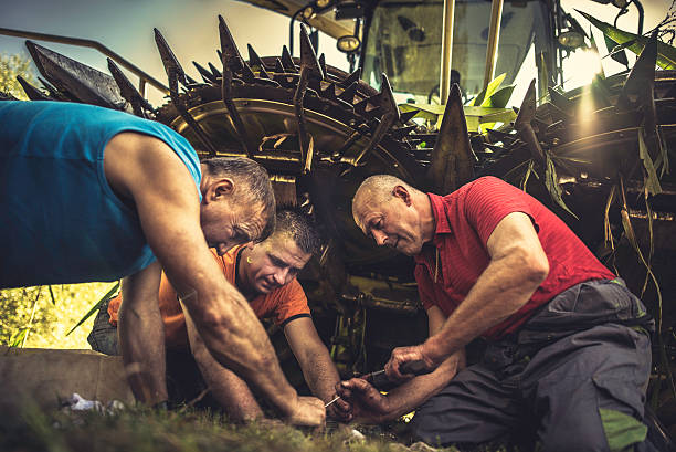 Senior farmer repairing parts of a combine while two others are assisting him.